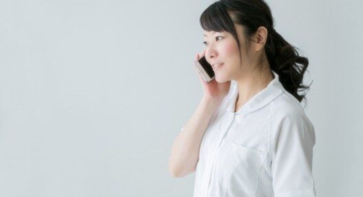 白衣姿の女性。右手で電話を耳に当てている。