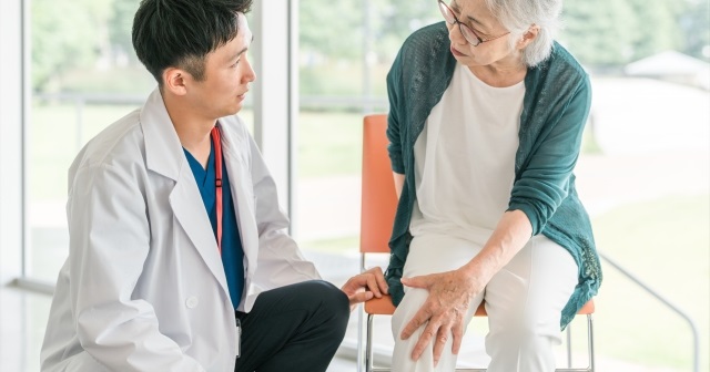 膝の痛みを訴える女性患者。親身になって傾聴する医療従事者。