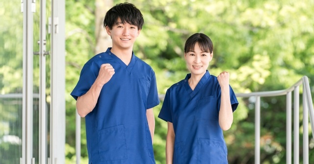 青いスクラブを着た男女。屋外でガッツポーズをとっている。