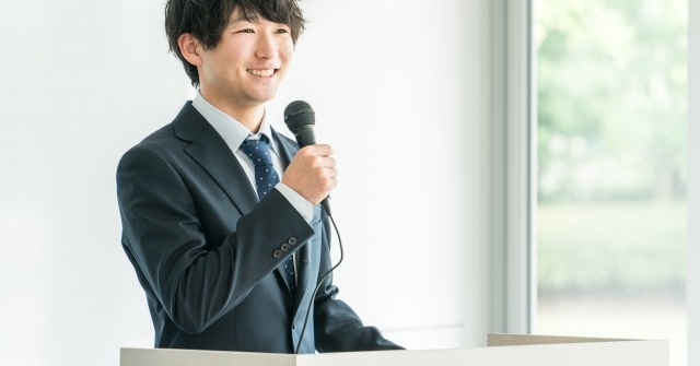 プレゼン中でマイクを持って話しているスーツ姿の男性