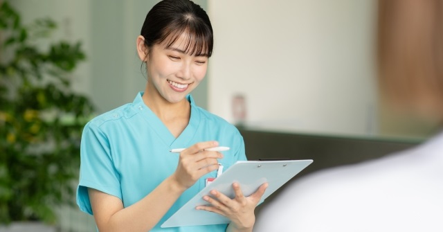 バインダを持つ白衣の女性。メモを取りレポートの準備に取り掛かる。