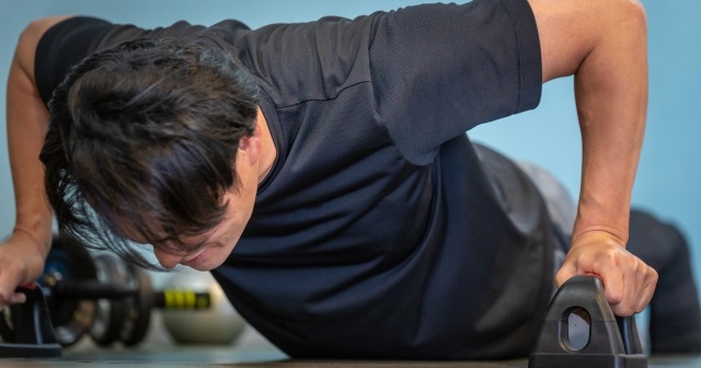 プッシュアップバーで腕立て伏せをする男性。