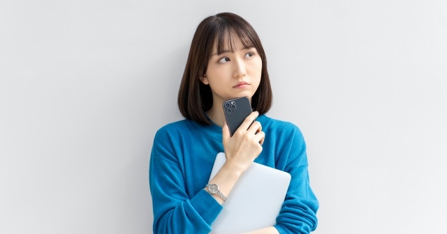 スマホを持ちながら考えごとをしている女性。