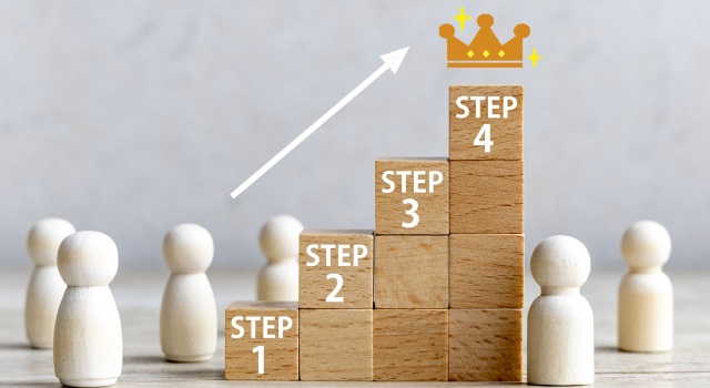積み上げた階段上の積木を昇ろうとする人形。積木にはSTEPの文字あり。